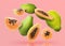 Cut and whole papaya fruits falling on pink background