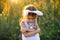 Cute 5-year-old girl with rabbit ears gently hugs a toy rabbit in nature in a blooming field in summer with golden sunlight.