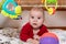 Cute 6 months little baby boy with curiosity expression on his face surrounded by colourful toys