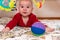 Cute 6 months little baby boy with curiosity expression on his face surrounded by colourful toys