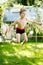 Cute active kid boy jumping in the garden on warm sunny summer day. Happy kid looking at the camera. Adorable child with