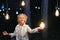 Cute adorable caucasian blond girl portrait smiling and holding in hand one of hanged edison light bulb at forest