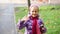 Cute adorable caucasian blond happy school girl smiling and waving hand in city park at warm autumn day. Cheerful child