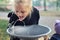 Cute adorable caucasian blond little thirsty school girl drinking water from public potable fountain faucet in city park