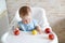 Cute adorable Caucasian child kid girl sitting in high chair eating apple fruit. Everyday lifestyle. Real authentic sweet home