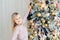 Cute adorable caucasian little blond smiling girl enjoy decorating christmas tree at home indoors. Happy child wearing pink