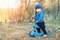 Cute adorable caucasian toddler boy in blue jacket having fun riding three-wheeled balance run bike scooter in city park or forest