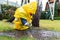 Cute adorable caucasian toddler boy in bright yellow raincoat and wellies playing alone at dirt muddy puddle during cold spring
