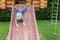 Cute adorable caucasian toddler boy having fun sliding down wooden slide at eco-friendly natural playground at backyard in autumn