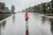 Cute adorable girl running splashing under rain on street road. Child having fun during rain shower storm. Seasonal summer