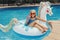 Cute adorable girl in sunglasses with drink lying on inflatable ring unicorn. Kid child enjoying having fun in swimming pool.