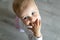 Cute adorable infant blond happy little toddler boy stand in home room looking above and sucking hand in mouth against floor