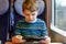 Cute adorable kid boy playing electronic games on tablet gadget during traveling by train. Happy child sitting near