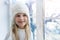 Cute adorable little blond beautiful cauasian girl stay near window, dream and looking outside waiting for snow, wonders