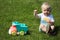 Cute adorable little child playing with toy car lorry on the green grass in the park