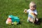 Cute adorable little child playing with toy car lorry on the green grass in the park