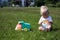 Cute adorable little child playing with toy car lorry on the green grass in the park