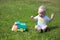 Cute adorable little child playing with toy car lorry on the green grass in the park