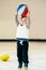 Cute adorable little small white Caucasian child toddler boy playing with ball basketball in gym on plain white light background