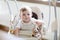 Cute adorable newborn baby girl sitting in swing indoors