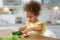 Cute African-American girl eating vegetables at table