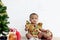 Cute African baby kid wears colorful dress and Sant hat, sits near beautiful decorative Christmas tree and present in white room,