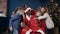 Cute african man in santa claus costume sitting on the chair and holding the gift while five kids running and hugging