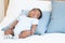 Cute African Nigerian newborn baby sleeping lying on pillow on white bed at home. Innocence infant with curly hair wear clothes