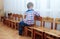 Cute alone caucasian baby boy with fair hair sits on the chair, back to the viewer, face to the window.