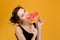 Cute amusing young woman biting sweet heart shaped lollipop