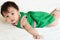 Cute Asian baby girl in a green dress is lying prone on a white bed in the bedroom