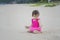 Cute Asian baby girl wearing pink color swimwear playing sands on the beach