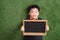 Cute asian child lying and holding blackboard on green grass