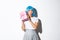 Cute asian girl in blue wig shaking box with gift, wonder whats inside, standing over white background