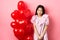 Cute asian girl in dress looking shy and smiling, standing modest near valentines day balloons, blushing on romantic
