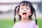 Cute Asian girl has dry and peeling lips. Children eat vitamin C orange color. Child opened his mouth wide. Kid braided two braids