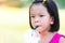 Cute Asian girl sucking water from a plastic glass with a green straw. On a hot day while she`s outside. Headshot