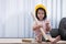 Cute Asian girl wearing a yellow toy hat like an engineer, she holds a roll of brown paper tube.
