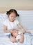 Cute Asian sister feeding milk from bottle for newborn baby lying on the bed