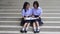 Cute Asian Thai high schoolgirls student couple in school uniform sit on the stairway discussing and reading homework or exam