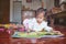 Cute Asian toddler girl child lying on her stomach while coloring with crayons in crafts book with sticker at home, Stay home Stay