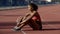 Cute athletic girl tired after workout at stadium sitting on track, resting