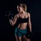 Cute athletic model girl in sportswear with dumbbells in studio against black background. Ideal female sports figure.