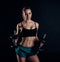 Cute athletic model girl in sportswear with dumbbells in studio against black background. Ideal female sports figure.