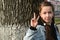 Cute attractive young girl shows her fingers the victory sign  v  background of the bark of large tree.