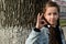 Cute attractive young girl shows OK sign with her fingers on background bark large tree.