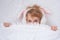 A cute baby appears from under a fluffy white blanket. Teenage girl with rabbit ears. Easter concept. Surprise