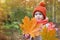Cute baby in autumn clothes. child in knitted hats and scarf holding orange maple leaves