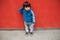 Cute baby in blue casual clothes standing in front of a red wall