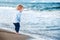 Cute baby boy on the beach, admiring the sea. Bare feet. Happy